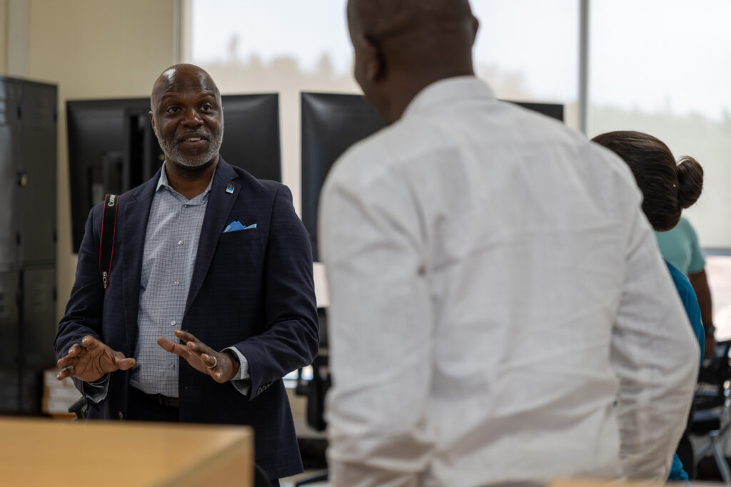 Man smiles in conversation with two other people in front of several computers.