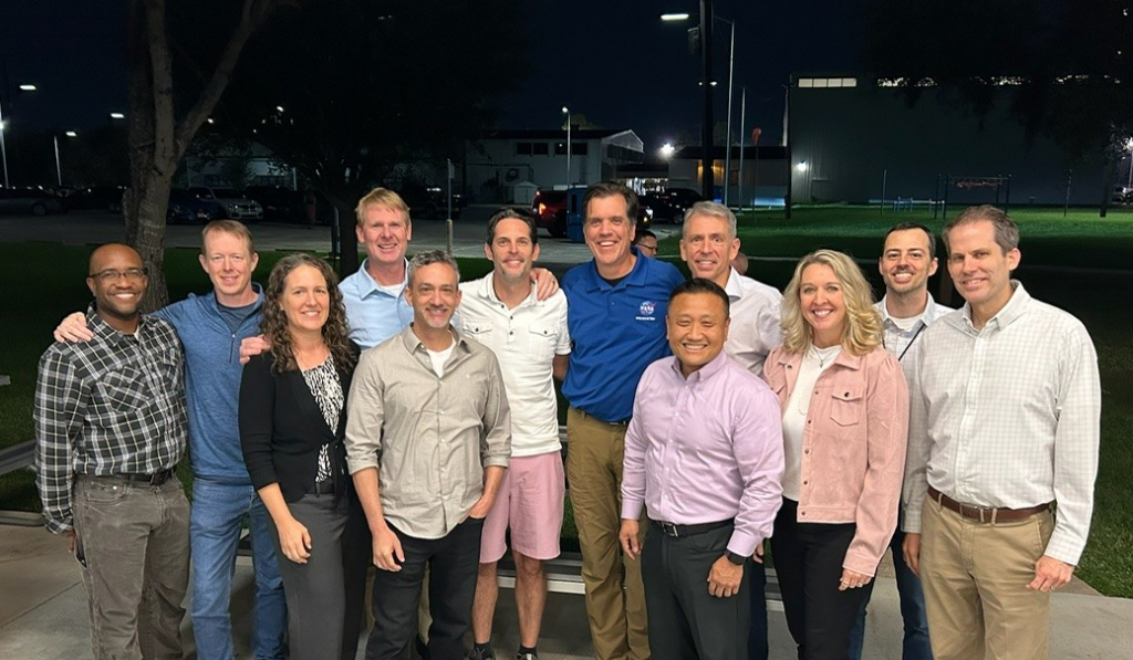 A dozen current and former NASA employees pose smiling outside.