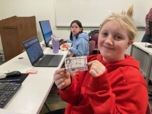Girls sits at a computer with a hand-drawn doodle that reads, "I love coding."