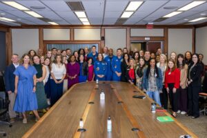 Four astronauts in flight suits pose with a group of professionals at Johnson Space Center